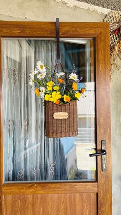 a basket filled with flowers sitting on top of a wooden door next to a window