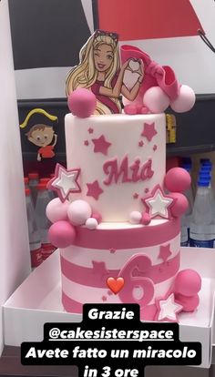 a pink and white cake with barbie dolls on it's top, in a store