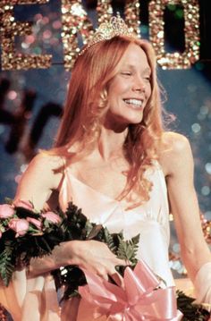 a woman wearing a tiara smiles as she stands in front of a stage backdrop