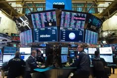 two men are standing in front of multiple screens on the floor of a stock market