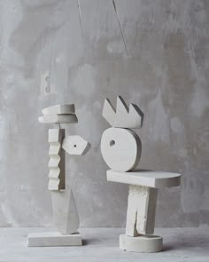 two sculptures made out of concrete are standing in front of a cement wall and one is holding a piece of wood