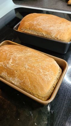 two loafs of bread sitting in pans on top of a counter next to each other