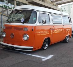 an orange and white vw bus parked in a parking lot next to a building