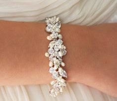 a woman's arm wearing a bracelet with white pearls and crystal stones on it