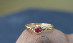 a gold ring with a red stone in it sitting on top of a piece of wood