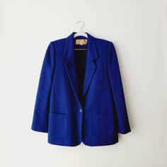 Cobalt blue and black longline wool blazer. The weave is a subtle herringbone pattern that looks like solid blue from far away, but gives dimension up close. 100% wool and fully lined.  Built-in shoulder pads give structure to this classic yet bold blazer. Has two front pockets, one chest pocket, and has a single front button closure and buttons at the sleeve cuffs.  Vintage size 8 - fits like large.  15 inches shoulder seam to shoulder seam,  18.5 inches across the chest,  27.5 inches top of sh Blue Tweed Office Jacket With Pockets, Blue Office Tweed Jacket With Pockets, Blue Single-breasted Tweed Jacket For Work, Blue Notch Lapel Tweed Jacket For Work, Blue Tweed Notch Lapel Jacket For Work, Blue Tweed Jacket With Notch Lapel For Work, Classic Blue Career Blazer, Blue Long Sleeve Tweed Jacket For Work, Blue Career Blazer For Fall