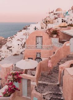 a woman is walking up the stairs to an old village by the ocean with umbrellas