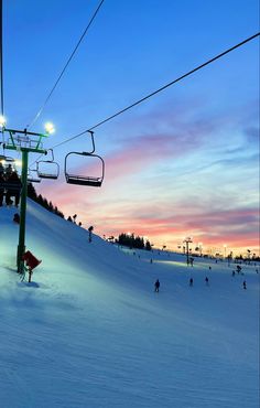 a ski lift with people skiing down the hill at sunset or dawn in the background