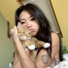 a woman with tattoos holding a cat in her arms and looking at the camera while sitting on a bed