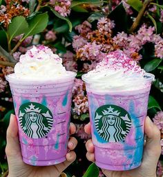 two people holding up starbucks drinks in front of some pink and purple flowers with sprinkles on them