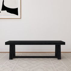 a black bench sitting in the middle of a room next to a wall with a painting on it