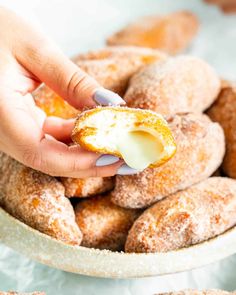 a person picking up a powdered sugar doughnut out of a white bowl with other donuts in the background