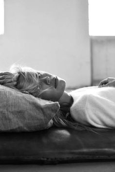 a black and white photo of a woman laying on a bed with her head resting on a pillow