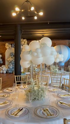 the table is set with white and gold plates, silverware, and balloon centerpieces