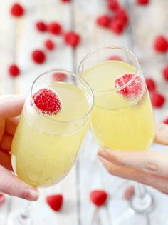 two people holding up glasses filled with liquid and raspberries on the rims