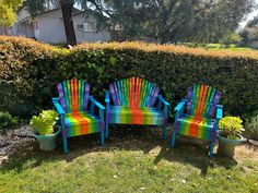 two colorful wooden chairs sitting next to each other on top of a grass covered field