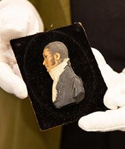 a man in white gloves holding a miniature portrait