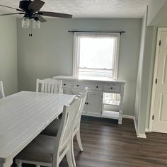 a white dining room table and chairs in front of a window with a ceiling fan