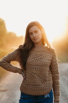 a woman standing on the side of a road wearing a brown crochet sweater