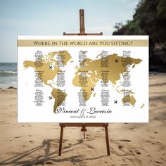 an easel on the beach with a world map in gold and white, which reads where in the world are you sitting?