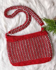 a crocheted red and white purse sitting on top of a fur rug next to a plant