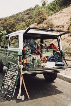 the back end of a pick up truck filled with luggage and camping gear sitting on the side of a road