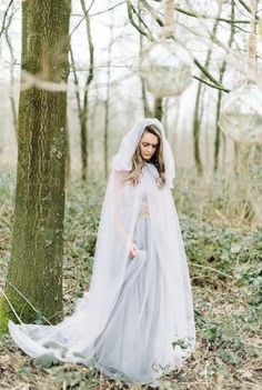 a woman wearing a veil and dress standing next to a tree in the middle of a forest