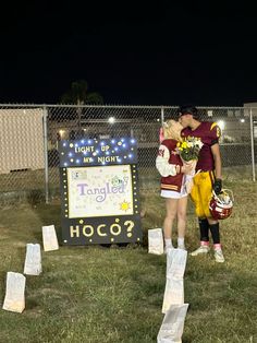 two people standing next to each other in front of a sign with flowers on it