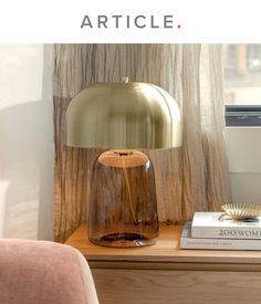 a table with a lamp, books and a book on it next to a window