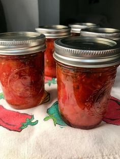 four jars of pickles sitting on top of a white table cloth with red peppers in them