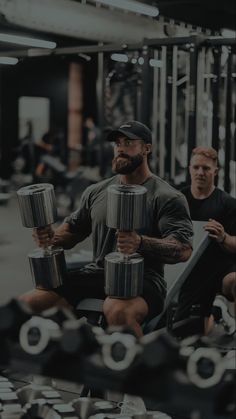 a man sitting in a gym holding two dumbs