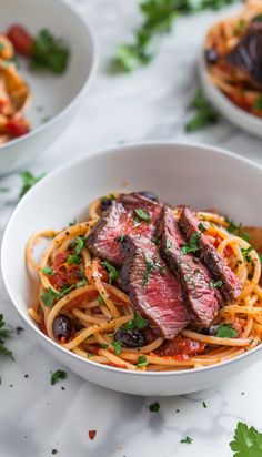 two white bowls filled with pasta and meat on top of a marble countertop next to other dishes