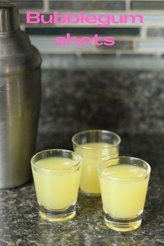 three shot glasses filled with bubblegum shots sitting on a counter next to a shaker