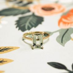 an emerald colored ring sitting on top of a flowered table cloth