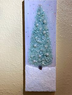 a small christmas tree in a glass block with snow on the bottom and pearls hanging from it