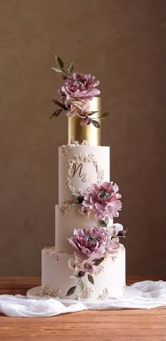 a three tiered wedding cake with pink flowers on the top and gold trimmings