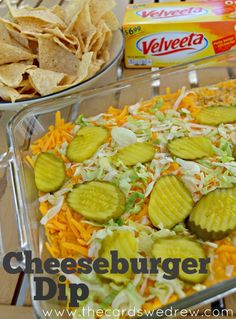 cheeseburger dip with chips and veggies in a glass dish on a wooden table