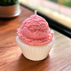 a cupcake with pink frosting sitting on top of a wooden table