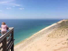 a woman sitting on top of a wooden bench next to the ocean near a beach