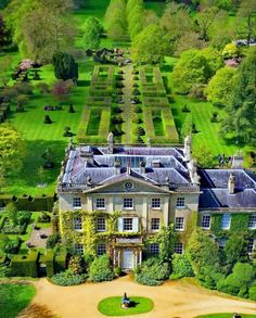 an aerial view of a large house surrounded by lush green trees and bushes with people sitting on the lawn