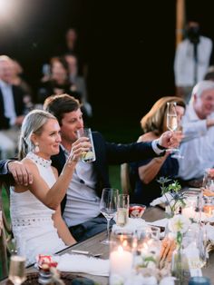 a bride and groom toasting with their friends at a dinner table in the evening