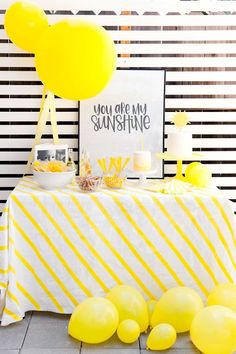 a table topped with yellow balloons next to a white and black striped cloth covered table