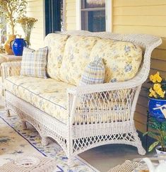 a white wicker couch sitting on top of a patio next to a yellow house