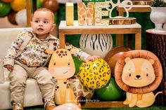 a little boy sitting on a couch next to stuffed animals and balloons in the shape of giraffes