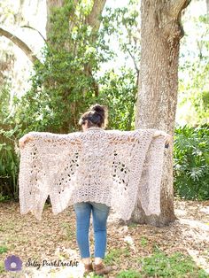 a woman standing in front of a tree holding a white crocheted shawl