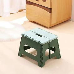 a green and blue step stool sitting on top of a white floor next to a wooden dresser