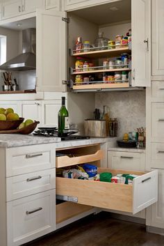 an open cabinet in the middle of a kitchen with white cupboards and drawers filled with food