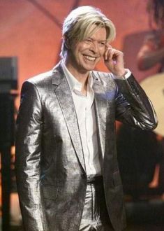 a man in a silver suit talking on a cell phone while holding his hand to his ear