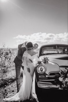 a bride and groom kissing in front of an old car on the side of the road