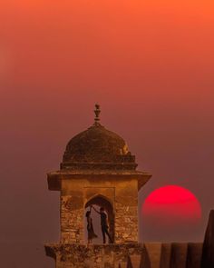 the sun is setting behind an old tower with a couple kissing in front of it